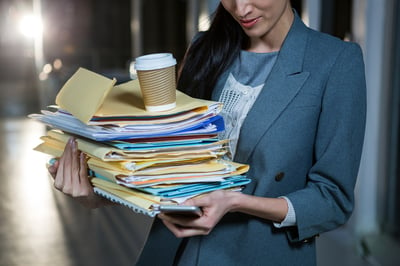 Businesswoman carrying stack of file folders while using mobile phone in the office
