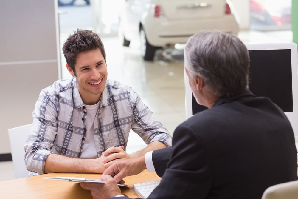 Salesman showing client where to sign the deal at new car showroom